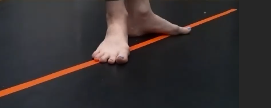 A close up photograph of Krishna's feet standing on an orange tape on the floor. 